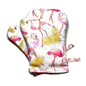 May include: A pair of white oven mitts with a pink flamingo and yellow palm leaf pattern on a white background with yellow polka dots.