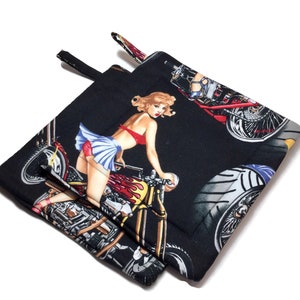 May include: Two black fabric pot holders with a pin-up girl and motorcycle design. The girl is wearing a red bikini top and a blue skirt. The motorcycle is red, yellow, and black.