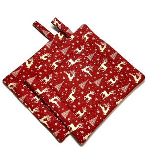 May include: Two red pot holders with a white reindeer and Christmas tree pattern. The pot holders have a loop handle.