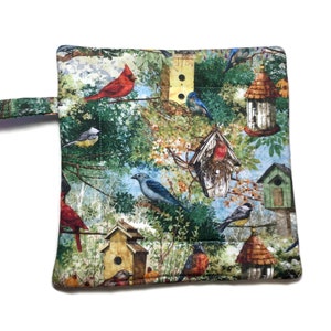 May include: A quilted pot holder with a colorful bird and birdhouse pattern. The pot holder has a loop handle and is made of fabric.