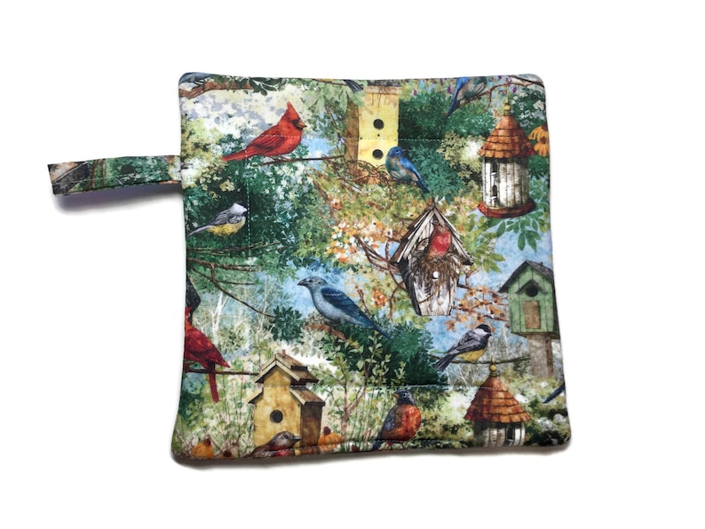 May include: A quilted pot holder with a colorful bird and birdhouse pattern. The pot holder has a loop handle and is made of fabric.