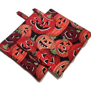Puede incluir: Dos agarraderas de cocina de color naranja y negro con temática de Halloween con un patrón de caras de calabaza.