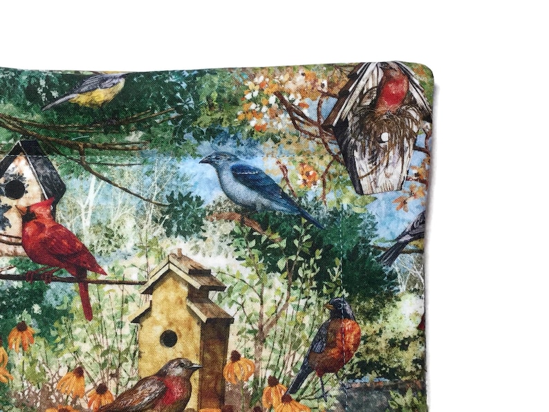 May include: A colorful fabric with a bird and birdhouse theme. The fabric features a variety of birds, including a blue jay, a cardinal, and a robin, perched on branches and in birdhouses. The background is a watercolor-style depiction of trees and leaves.