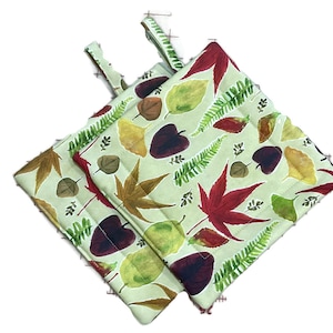 May include: Two green pot holders with a fall leaf pattern. The pot holders have a loop handle and are made of fabric.