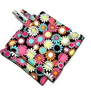 May include: Two black pot holders with a colorful daisy print. The daisies are pink, blue, yellow, and orange on a black background.