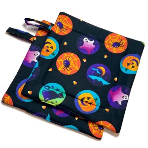 Puede incluir: Dos agarraderas de cocina negras con temática de Halloween con diseños coloridos de calabazas, fantasmas, arañas, murciélagos y maíz dulce.