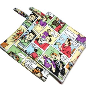 Puede incluir: Dos agarraderas de olla coloridas con un diseño de cómic. Las agarraderas tienen un fondo amarillo con contornos negros y acentos rojos, azules, verdes, morados y rosas. El texto en las agarraderas dice "Dysfunctional Family by Michael Muller".