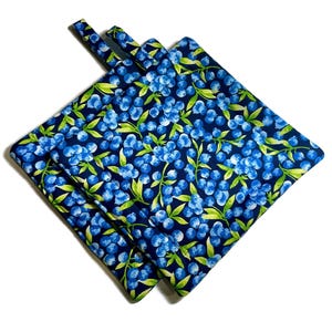 May include: Two blue and green pot holders with a blueberry pattern. The pot holders are made of fabric and have a loop handle.