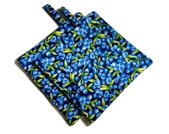 May include: Two blue and green pot holders with a blueberry pattern. The pot holders are made of fabric and have a loop handle.