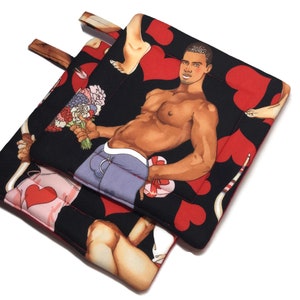 May include: Two black pot holders with a red heart pattern. One pot holder features a man holding a bouquet of flowers and a gift box. The other pot holder features a pair of legs and a tail.