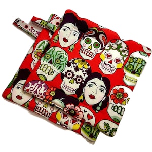 Puede incluir: Bolsas de tela rojas con un patrón repetido de calaveras de azúcar y retratos de Frida Kahlo. Las bolsas tienen diseños florales y geométricos coloridos. Las bolsas están hechas de tela y tienen lazos de tela.