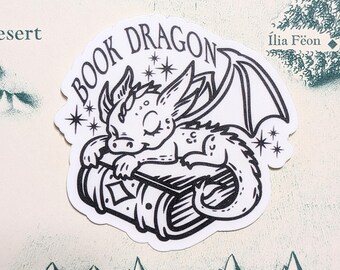 May include: A black and white sticker of a sleeping dragon on a book, with the words "BOOK DRAGON". The sticker is set against a map background with mountains and text, creating a fantasy theme.