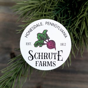 May include: A white circular sticker with the text "Honesdale, Pennsylvania" and "Schrute Farms" in black. The sticker features a beet graphic with green leaves and a purple root. The year "1812" is also printed on the sticker.