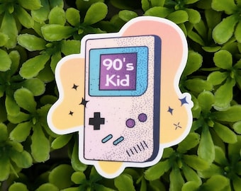 May include: A sticker featuring a retro handheld game console design with the text "90's Kid" on the screen. The sticker has a white border and a pastel color scheme of pink, yellow, and blue, with star accents.