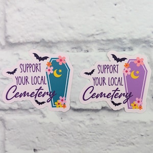 Pode incluir: Dois adesivos com um design de caixão e o texto "Apoie o seu cemitério local". Um adesivo tem um caixão roxo com flores rosa e uma lua crescente. O outro adesivo tem um caixão azul com flores rosa e uma lua crescente.
