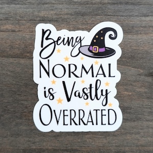 May include: A white sticker with the text "Being NORMAL is Vastly OVERRATED" in black script and block letters. A witch's hat with a purple band and gold stars is above the word "NORMAL".