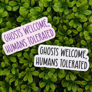 May include: Two white stickers with purple text on a green background. The text on the stickers reads "Ghosts Welcome, Humans Tolerated".