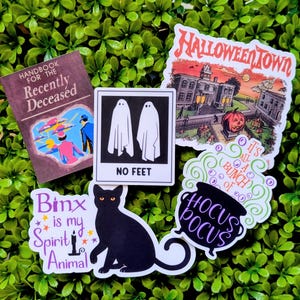 May include: A collection of five Halloween-themed stickers featuring a Handbook for the Recently Deceased book cover, two white ghosts with the text NO FEET, a Halloweentown scene, a black cat with Binx is my Spirit Animal text, and a Hocus Pocus cauldron.