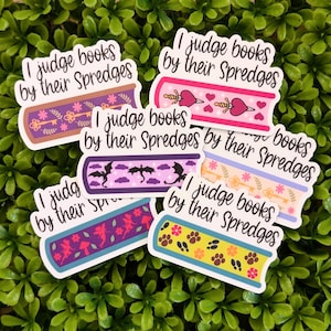 Op de afbeelding: Een verzameling stickers met een boeken thema, elk met de tekst "I judge books by their Spredges". De stickers hebben verschillende ontwerpen, waaronder sleutels, harten, draken en pootafdrukken, met een witte rand.