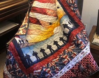 May include: A red, white, and blue patriotic quilt with a silhouette of soldiers and helicopters. The quilt has a border of American flags and the words "Loyalty, Strength, and Courage".