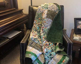 May include: A green and white patchwork quilt with a variety of patterns, including trees, animals, and geometric shapes. The quilt is folded and draped over a brown leather armchair.