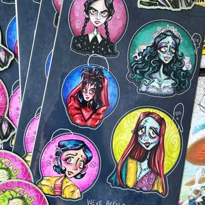 May include: A set of 6 round stickers featuring various cartoon characters with a black background. The characters include Wednesday Addams, Sally from The Nightmare Before Christmas, and a bride with a white dress and a crown. The stickers have a pink, yellow, blue, and green background. The text on the stickers reads "We've been dying 2 meet u! Summer Purks.com".