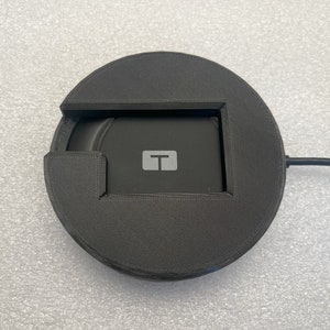 May include: A black wireless charging pad with a small rectangular cutout in the center. The charging pad has a black cord attached to it.