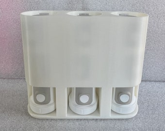 Op de afbeelding: Witte plastic dispenser met drie compartimenten voor het bewaren van kleine voorwerpen. Elk compartiment heeft een afneembaar deksel en een witte knop aan de voorkant.