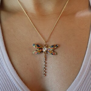 Puede incluir: Un collar de oro con un colgante de lib&eacute;lula colorido y una cadena colgante de diamantes de imitaci&oacute;n transparentes.