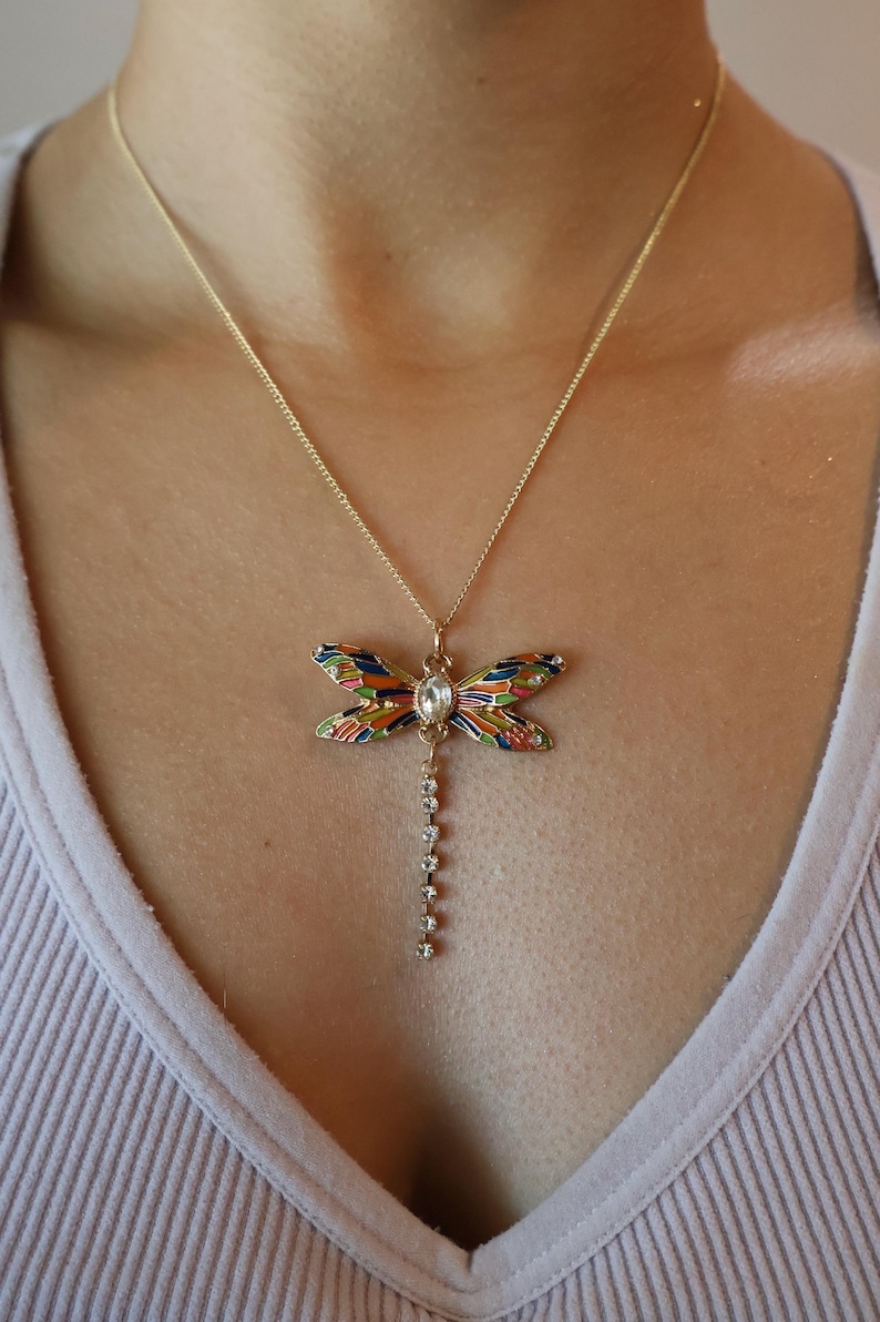 Puede incluir: Un collar de oro con un colgante de lib&eacute;lula colorido y una cadena colgante de diamantes de imitaci&oacute;n transparentes.