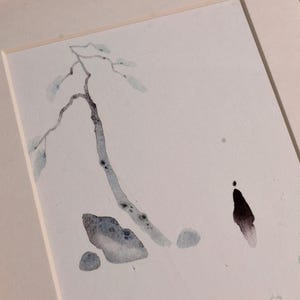 Op de afbeelding: Aquarel schilderij van een boomtak met bladeren en een figuur, in een houten lijst. Het kunstwerk toont gedempte blauw- en grijstinten op een witte achtergrond. De lijst is lichtbruin.