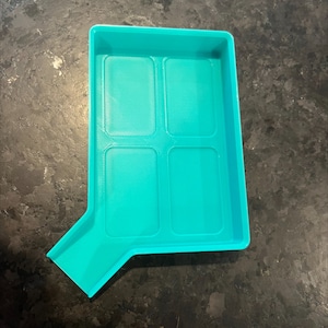 May include: A turquoise blue plastic tray with four rectangular compartments and a spout on one side. The tray is designed for organizing small items.