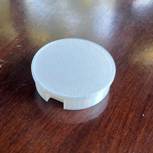 May include: A white plastic round lid with a textured surface and three small tabs on the bottom.