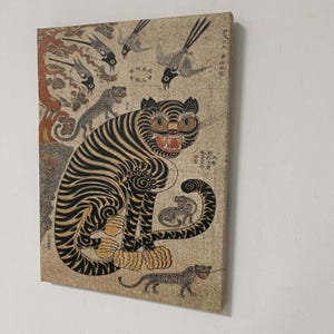 May include: A vintage canvas print featuring a tiger with black stripes and yellow eyes, surrounded by other tigers and birds. The artwork has a traditional Asian style with faded colors and intricate details.