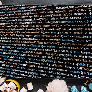 May include: A black canvas print displaying white computer code, set against a backdrop of a cream-coloured knitted blanket. A mug of hot chocolate with marshmallows and winter decorations adds a festive touch.