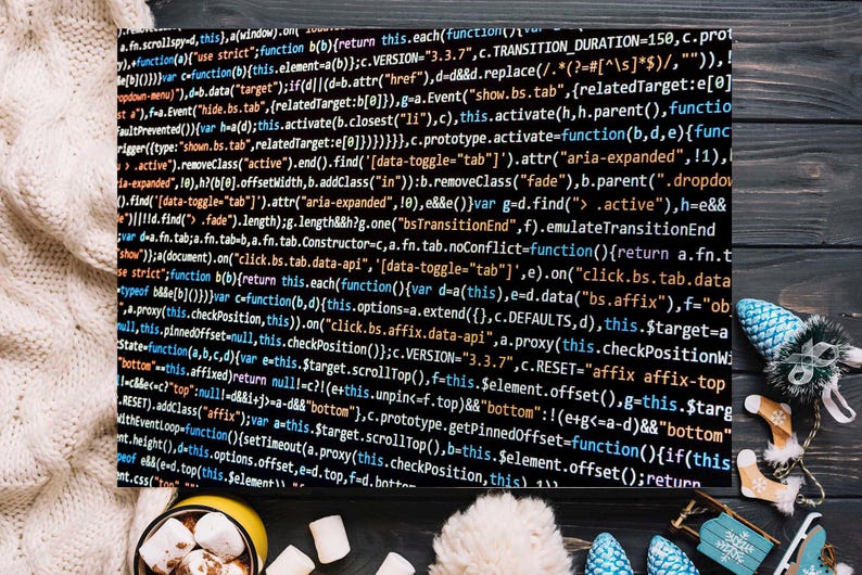 May include: A black canvas print displaying white computer code, set against a backdrop of a cream-coloured knitted blanket. A mug of hot chocolate with marshmallows and winter decorations adds a festive touch.