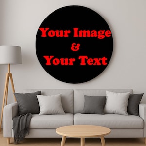 Op de afbeelding: Een groot, rond zwart wandkunstwerk met rode tekst die luidt "Your Image & Your Text". Het kunstwerk hangt boven een lichtgrijze bank met kussens en een houten salontafel. Een staande lamp staat links.
