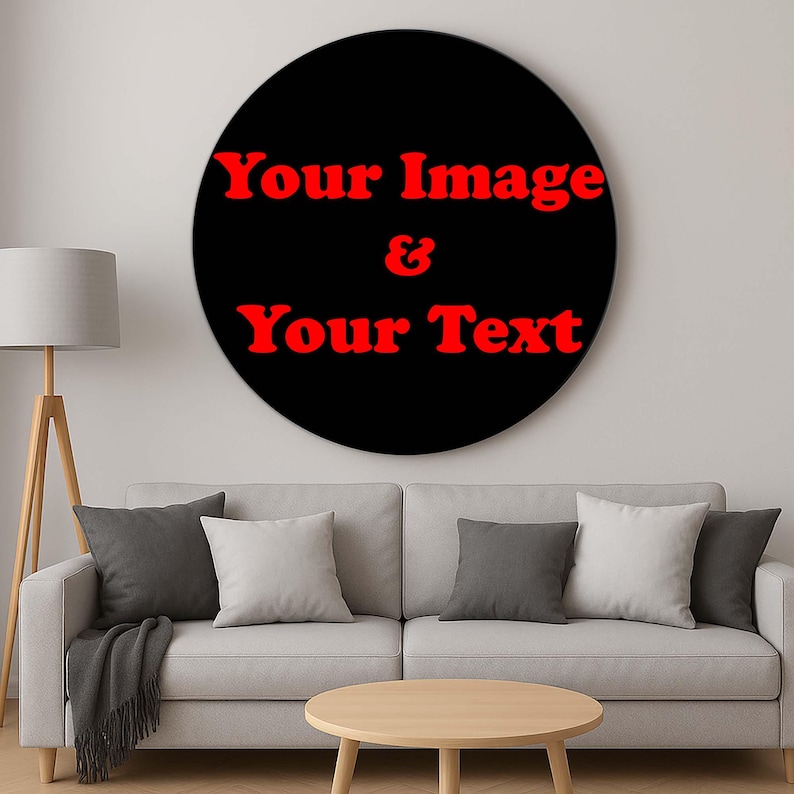 Op de afbeelding: Een groot, rond zwart wandkunstwerk met rode tekst die luidt "Your Image & Your Text". Het kunstwerk hangt boven een lichtgrijze bank met kussens en een houten salontafel. Een staande lamp staat links.