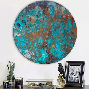 Op de afbeelding: Een groot, rond kunstwerk voor aan de muur met een textuur. Het kunstwerk toont een mix van turquoise, bruine en koperkleuren, wat een abstracte, verweerde uitstraling geeft. Het is aan een witte muur bevestigd, met decoratieve items op een donkere ondergrond.