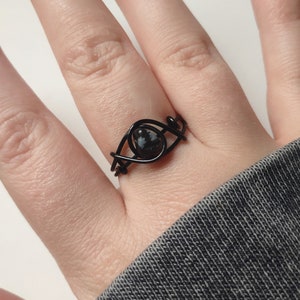 May include: A black wire wrapped ring with a black and white stone in the center.