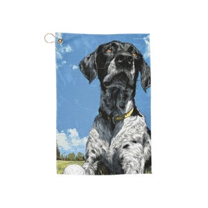 Könnte beinhalten: Golfhandtuch mit einer detaillierten Illustration eines Hundes mit schwarz-weißem Fell, der einen gelben Kragen trägt und nach oben blickt. Der Hintergrund zeigt einen blauen Himmel mit Wolken und einen Golfball auf dem Grün.