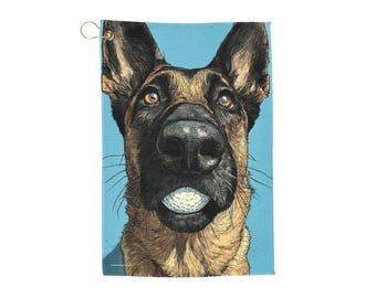 May include: Golf towel featuring a detailed illustration of a German Shepherd with a golf ball in its mouth. The dog's fur is brown and black, set against a light blue background. Includes a gold-colored metal loop for hanging.
