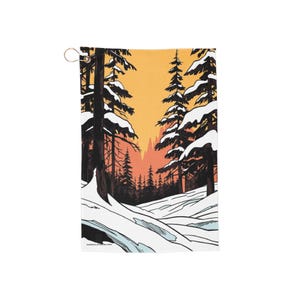 May include: A rectangular golf towel depicting a winter scene with snow-laden trees and a sunset. The design includes a snowy foreground, dark tree trunks, and a vibrant orange and yellow sky. A metal ring is attached at the top.