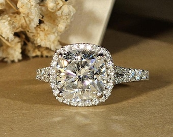 May include: A square-shaped diamond engagement ring with a halo setting. The ring is set in white gold and features a row of smaller diamonds on each side of the centre stone.