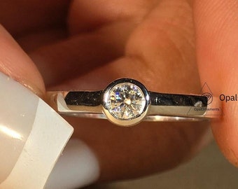 Puede incluir: Un anillo de banda de plata simple con una sola piedra preciosa redonda transparente engastada en bisel.