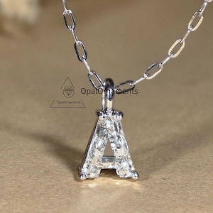 Pode incluir: Um colar de corrente de prata com um pingente em forma da letra A. A letra é feita de pequenos diamantes.
