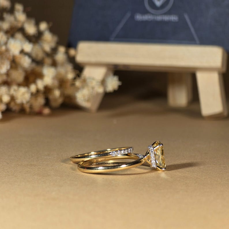 May include: A set of two gold wedding bands with a yellow gemstone in the center of the larger band. The larger band has a row of small diamonds around the gemstone.