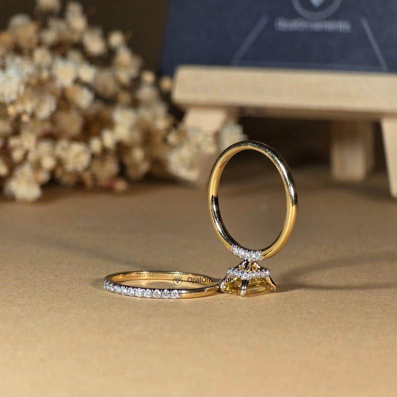 May include: A yellow gold engagement ring set with a center stone and a matching band. The center stone is a yellow diamond with a triangular shape. The band is a thin band with small diamonds set in a pave setting.