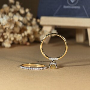 May include: A set of two gold wedding bands with a yellow gemstone and small diamonds. The larger band has a single yellow gemstone in the center with a halo of small diamonds. The smaller band has a row of small diamonds around the band.