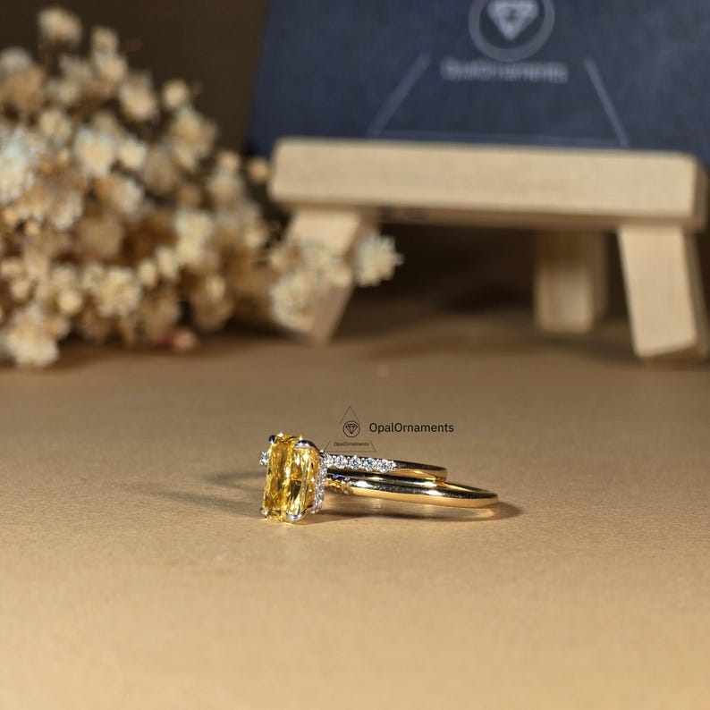 May include: A yellow gemstone engagement ring with a matching band. The ring is set in gold and features a rectangular cut gemstone surrounded by smaller diamonds.